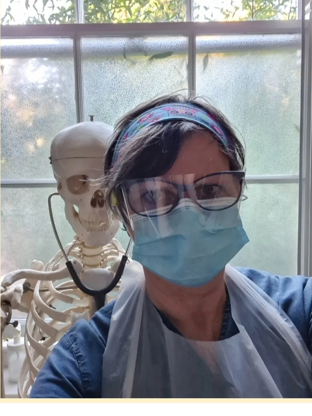 Clare in mask, visor and apron next to the clinic skeleton